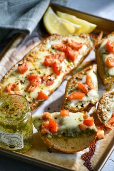 bread with tomatoes, cheese and pesto sauce on it next to lemon wedges