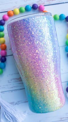 a purple and blue glitter cup sitting on top of a white table next to beads