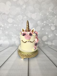 a white cake with pink flowers and a unicorn horn on it's top sitting on a wooden table