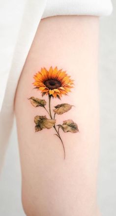 a small sunflower tattoo on the right side of the thigh, with leaves around it