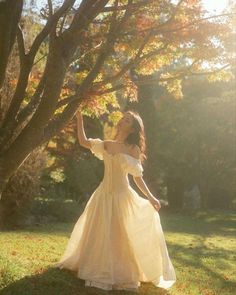 a woman in a white dress is standing under a tree with her hand up to the sky