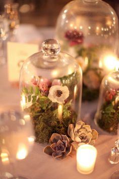 several glass domes with flowers and candles on a table