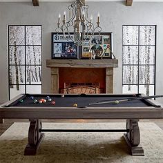 a pool table in front of a fireplace with chandelier and pictures on the wall