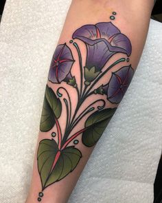 a woman's arm with purple flowers and green leaves on the left side of her leg