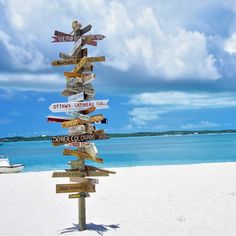 a sign post on the beach with many signs pointing in different directions to various destinations