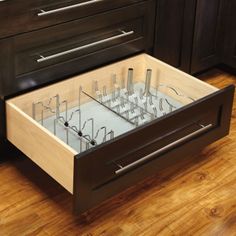 an open drawer in the middle of a kitchen with wooden flooring and dark cabinets