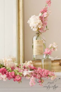 pink and white flowers in a glass vase on a mantle with a mirror behind it