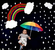 a baby is holding an umbrella in front of a rainbow and rain scene with clouds