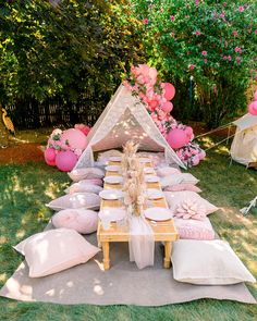 a table set up for a party with pink and white balloons, pillows and decorations