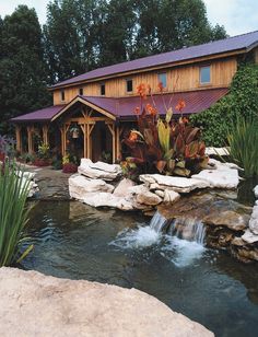 a house sitting on top of a lush green hillside next to a small waterfall in front of it