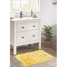 a white bathroom vanity with yellow rug on the floor next to it and a potted plant