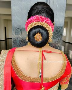 the back of a woman's head wearing a red and gold saree with flowers in her hair