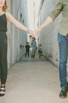 two people holding hands while walking down an alley way with other people in the background