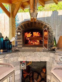 an outdoor pizza oven with wood burning in it's center and lots of firewood