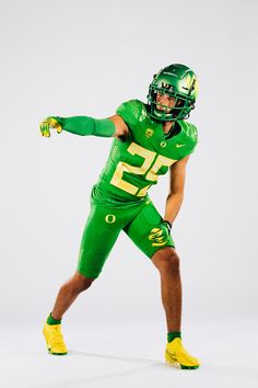 a football player in green and yellow uniform holding his arm out to the side with both hands