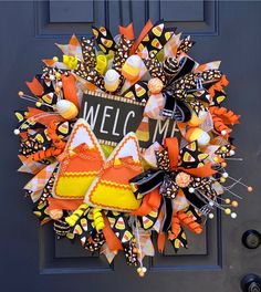 a welcome wreath with orange and yellow decorations on the front door for someone's house