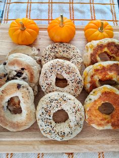 a wooden cutting board topped with bagels and doughnuts next to mini pumpkins