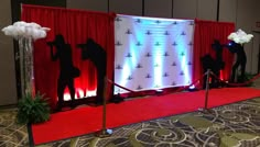 a red carpeted area with white and blue lights on the walls, two black silhouettes in front of a red curtain