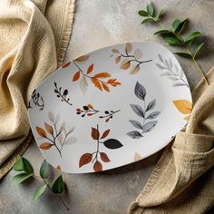 a plate with leaves painted on it next to some cloths and green plants in the background