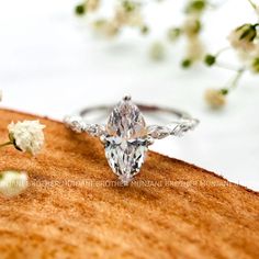 a diamond ring sitting on top of a piece of wood with flowers in the background