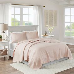 a bedroom with white bedding and windows in the background, including a rug on the floor