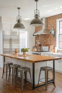 A kitchen with a rustic brick backsplash, stainless steel appliances, and large industrial pendant lights over a wooden island. Exposed Brick Backsplash, Brick Backsplash Kitchen, Brick Kitchen, Brick Backsplash, Backsplash Kitchen, The Judge, Red Bricks, Industrial Lighting