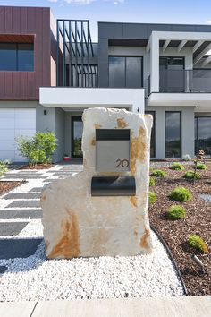 a large rock with a house number on it in front of some bushes and trees