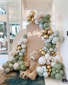 a teddy bear sitting in front of a giant balloon arch with gold and white balloons