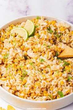 a white bowl filled with rice and corn next to sliced limes on the side