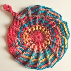 a crocheted hat is shown on a white surface with red, yellow and blue yarn