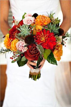 a woman holding a bouquet of flowers in her hands and wearing a white dress with red, orange, yellow and green accents