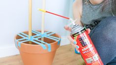 a woman sitting on the floor with a can of paint next to a potted plant