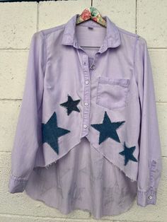 a purple shirt with blue stars is hanging on a white brick wall and has a pink flower in it