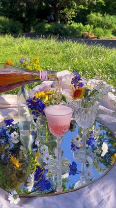 there is a tray with glasses and flowers on the table in front of some grass