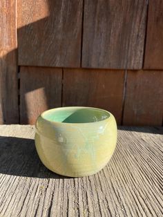 a small green bowl sitting on top of a wooden table next to a wall with wood slats