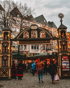 people are walking around in front of the entrance to a christmas market with lights on