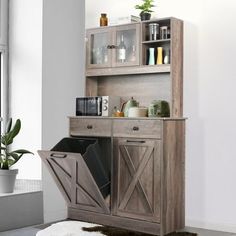 a kitchen area with a wooden cabinet and black trash can on the floor next to a potted plant