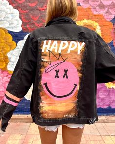 a woman wearing a jean jacket with the words happy painted on it