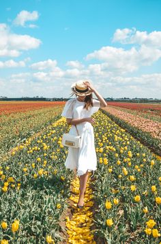 a woman in a white dress and straw hat walks through a field with yellow flowers