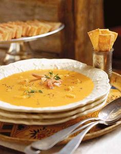 there is a bowl of soup on the table with crackers and bread in the background