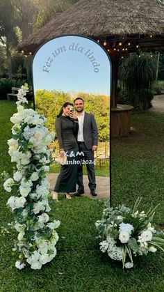 a man and woman standing in front of a mirror with flowers on the ground next to it