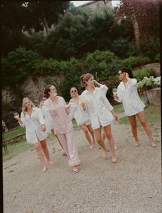 a group of women walking down a dirt road next to each other in white dresses