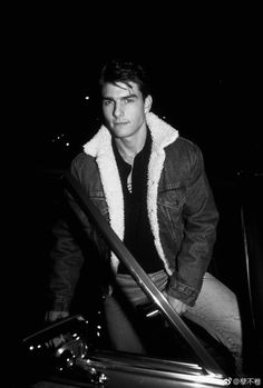 black and white photograph of a man sitting on a car with his hand in the door handle