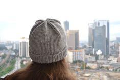 a woman with long hair wearing a hat looking out over a cityscape in the distance