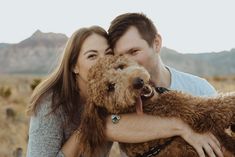 a man and woman hugging their dog in the desert