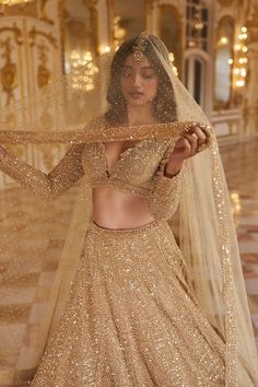 a woman in a gold lehenga and veil is posing for the camera with her hands on her hips