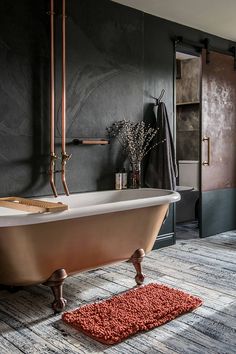 a bath tub sitting on top of a wooden floor next to a rug in front of a window