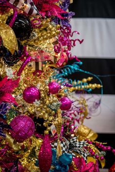 a colorful christmas tree decorated with ornaments and ribbons in pink, blue, gold and black colors