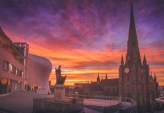 the sun is setting over an old city with spires and buildings in the foreground