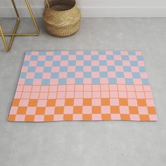 an orange and blue checkered rug on the floor next to a basket with a plant in it